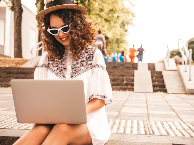 Bela modelo sorridente com afro cachos penteado vestido com vestido branco hipster de verão.