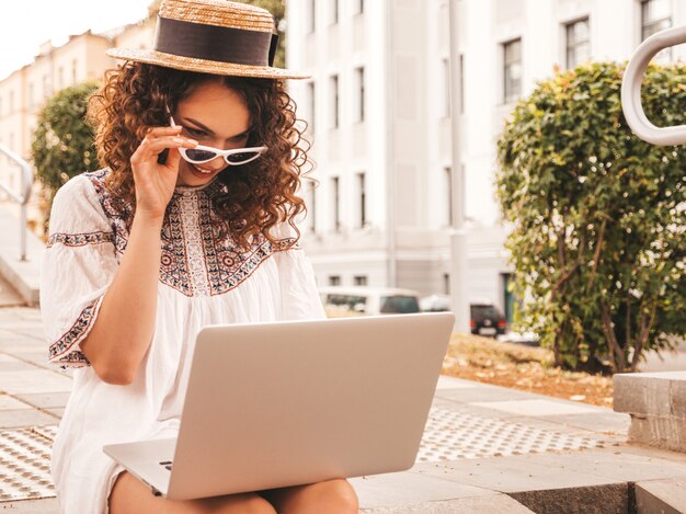 Bela modelo sorridente com afro cachos penteado vestido com vestido branco hipster de verão.