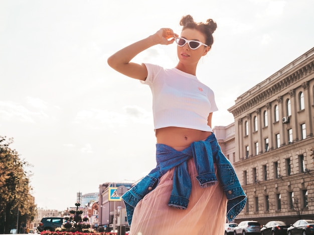 Bela modelo sorridente com penteado de chifres, vestido com roupas de jeans de jaqueta hipster de verão. garota despreocupada sexy, posando na rua. mulher na moda engraçada e positiva, se divertindo em óculos de sol