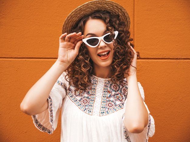 Bela modelo sorridente com penteados de cachos afro, vestida com óculos de sol e vestido branco hipster de verão