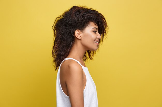 Bela mulher afro-americana atraente com óculos na moda postagem sobre o fundo amarelo do estúdio. Espaço de cópia.