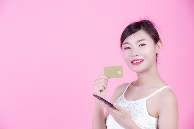 Bela mulher segurando um smartphone e cartão em um fundo rosa