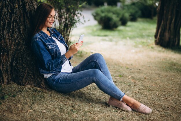 Bela mulher sentada debaixo de uma árvore e falando ao telefone