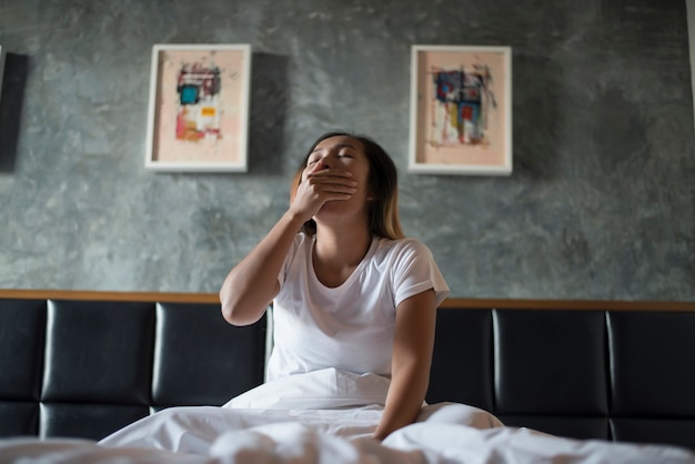 Foto grátis bela mulher sentada na cama e bocejando no quarto