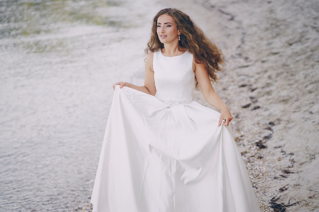 Bela noiva de cabelos compridos em um magnífico vestido branco caminhando na praia
