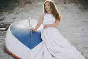Foto grátis bela noiva de cabelos compridos em um magnífico vestido branco sentado perto de barco