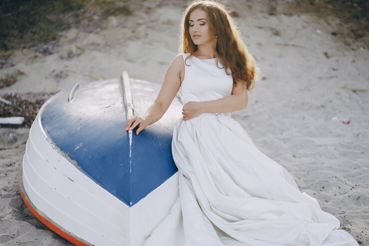 Foto grátis bela noiva de cabelos compridos em um magnífico vestido branco sentado perto de barco