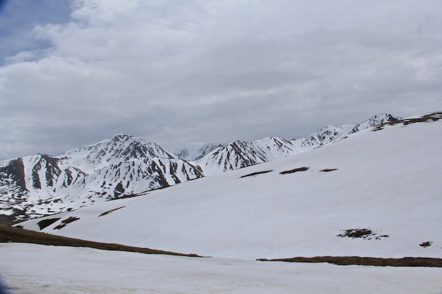 Bela paisagem de altas montanhas rochosas cobertas de neve sob um céu nublado