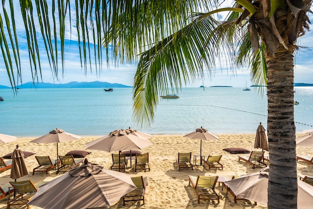 Bela praia tropical mar e oceano com palmeira de coco e guarda-chuva e cadeira no céu azul e nuvem branca
