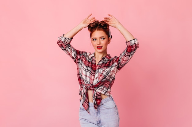 Bela senhora pinup olhando para a câmera. jovem gengibre confiante em camisa quadriculada, posando com as mãos para cima.