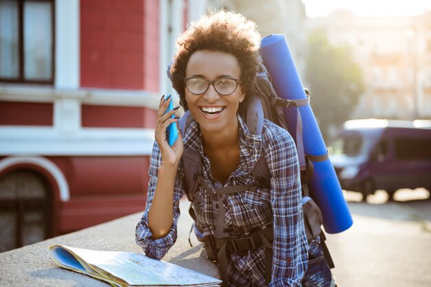 Bela viajante feminino Africano com mochila, falando no telefone, sorrindo.