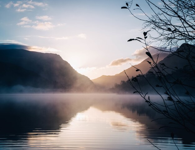 Bela vista de um lago rodeado por montanhas com um sol brilhante ao fundo