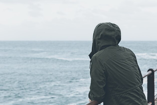 Bela vista de uma pessoa de pé na doca olhando para o oceano em um tempo nublado