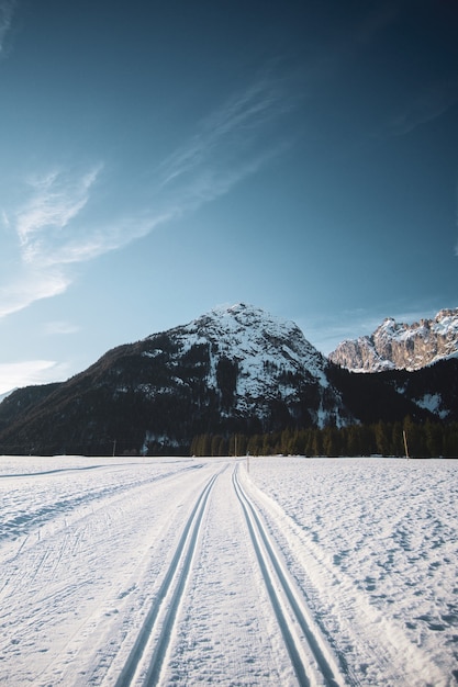 Bela vista do céu azul com montanhas e uma estrada cheia de neve com marcas de pneus durante o inverno