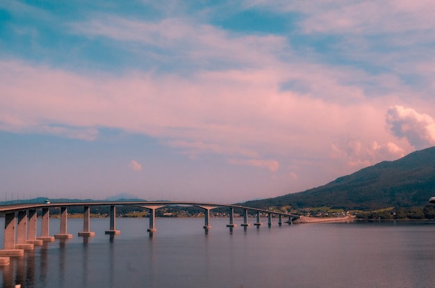 Belas paisagens de uma ponte de concreto sobre o lago perto de altas montanhas durante o pôr do sol na Noruega