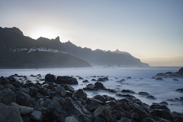 Belas pedras na praia à beira-mar nevoento com as montanhas