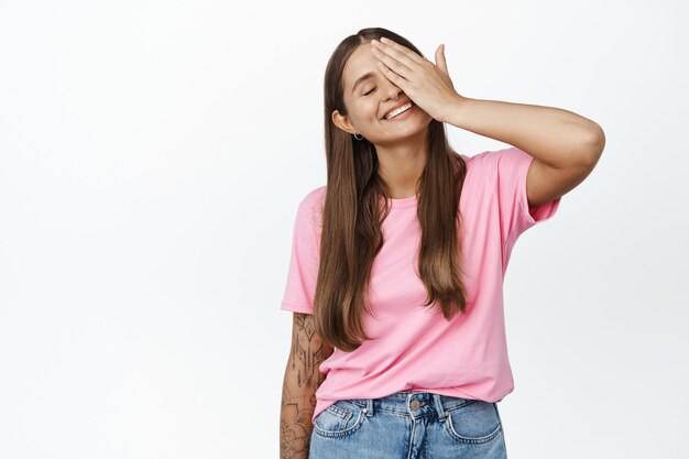 Beleza. A modelo feminina despreocupada atinge um lado do rosto, toca a pele do rosto com os olhos fechados e satisfeitos, sorriso romântico no branco