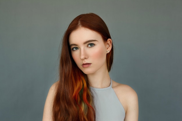 Beleza, cuidados com a pele, juventude, estilo e moda. deslumbrante e tenro modelo de mulher jovem com cabelo longo encaracolado colorido com mechas isoladas na parede cinza em branco, olhando