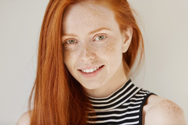 Beleza e cuidados com a pele. Retrato altamente detalhado de atraente ruiva adolescente com sorriso encantador e sardas fofas, descansando dentro de casa com o cabelo solto. Mulher linda relaxando em casa