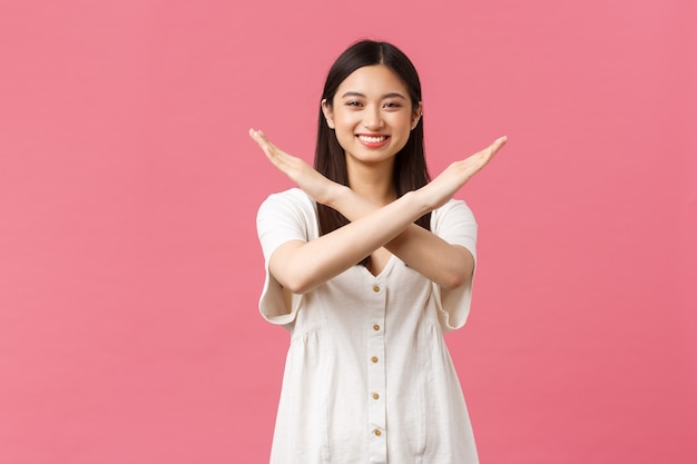 Foto grátis beleza, emoções das pessoas e conceito de lazer de verão. menina asiática sorridente alegre pedindo educadamente para parar, mostrar o sinal da cruz na proibição e proibir, sorrindo feliz, em pé fundo rosa.