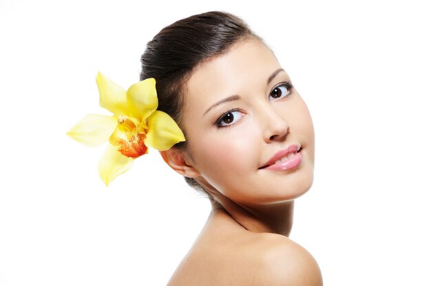 Beleza sorridente rosto feminino com orquídea amarela na orelha - sobre branco