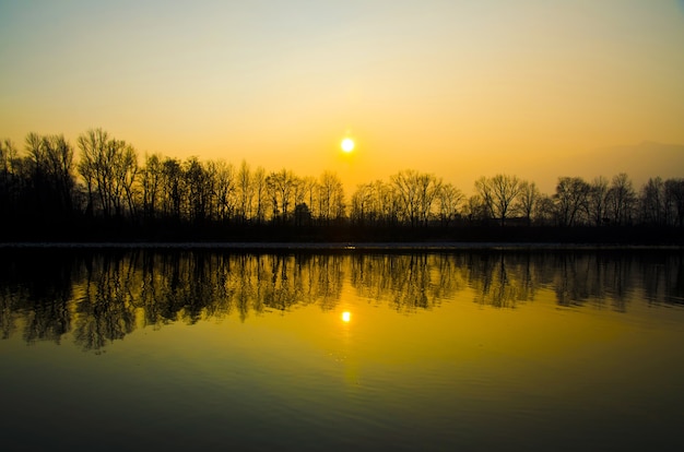 Belo cenário de pôr do sol sobre o lago com silhuetas de árvores refletidas na água