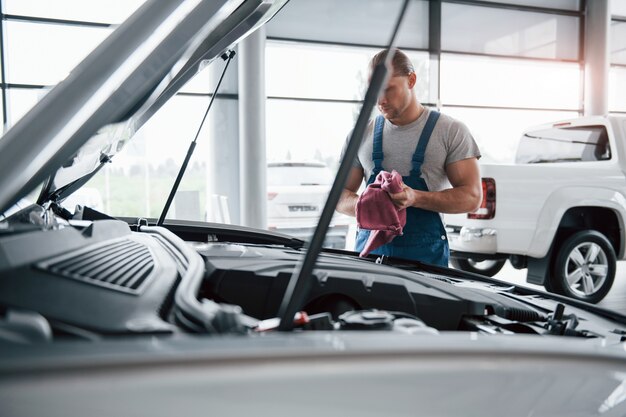 Belo dia. Homem de uniforme azul trabalha com carro quebrado. Fazendo reparos