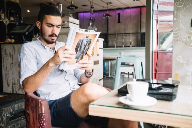 Belo homem relaxante com revista no café