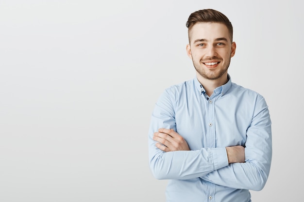 Belo jovem empresário com braços cruzados e sorrindo confiante