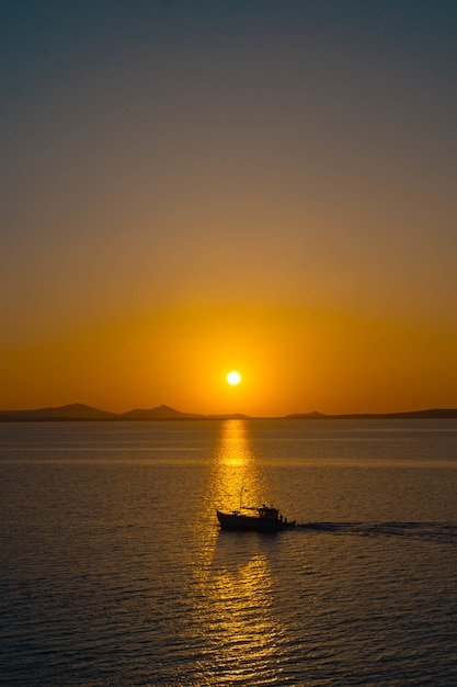 Belo oceano com um pequeno barco flutuando na água ao pôr do sol