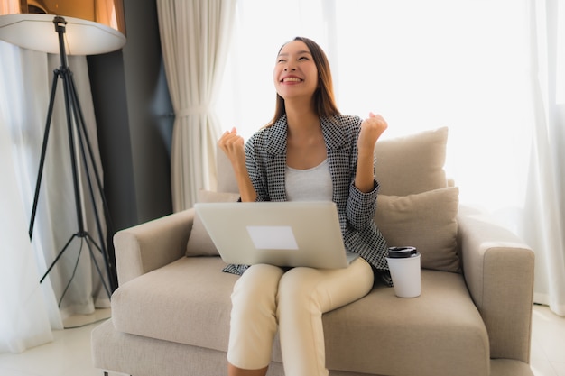 Belo retrato asiático jovem usando computador e laptop com uma xícara de café, sentado no sofá