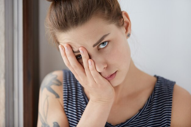 Belo retrato de mulher entediada, descansando metade do rosto na palma da mão. Garota atraente com cabelos castanhos e olhos azuis, cansada de conversas complicadas, tentando se esconder de uma conversa maçante debaixo do braço.