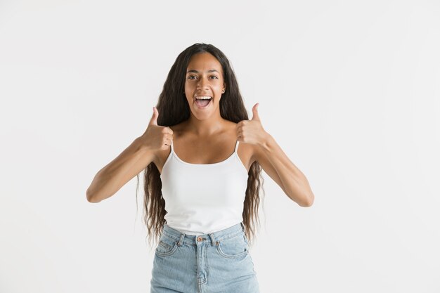 Belo retrato feminino com metade do comprimento em fundo branco do estúdio. Jovem emocional afro-americana com cabelo comprido. Expressão facial, conceito de emoções humanas. Mostrando sinal de legal ou ótimo.