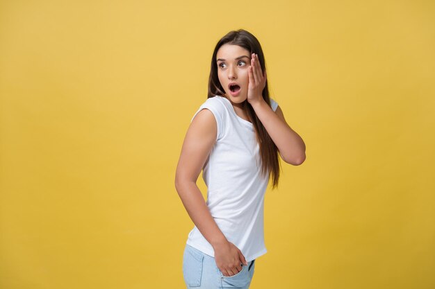 Belo retrato feminino de meio comprimento isolado em backgroud de estúdio amarelo A jovem emocional sorridente e surpresa mulher de pé e olhando para a câmeraO conceito de expressão facial de emoções humanas