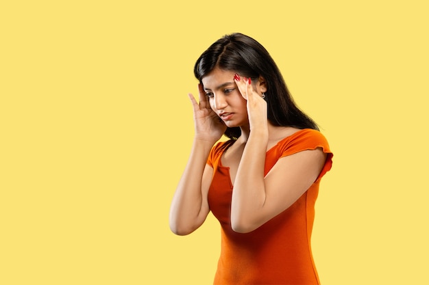 Belo retrato feminino de meio comprimento isolado no espaço amarelo. Jovem indiana emocional em um vestido pensativo ou sofrendo de dor