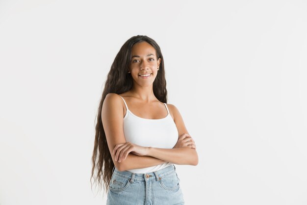 Belo retrato feminino de meio comprimento isolado no fundo branco do estúdio. Jovem emocional afro-americana com cabelo comprido. Expressão facial, conceito de emoções humanas. De pé e sorrindo.