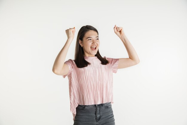 Belo retrato feminino de meio comprimento isolado no fundo branco do estúdio. Jovem mulher emocional com roupas casuais. Emoções humanas, conceito de expressão facial. Comemorando como vencedor, parece feliz.