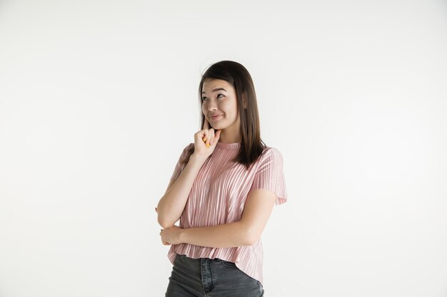 Belo retrato feminino de meio comprimento isolado no fundo branco do estúdio. Jovem mulher emocional com roupas casuais. Emoções humanas, conceito de expressão facial. Pensa ou sonha, parece pensativo.