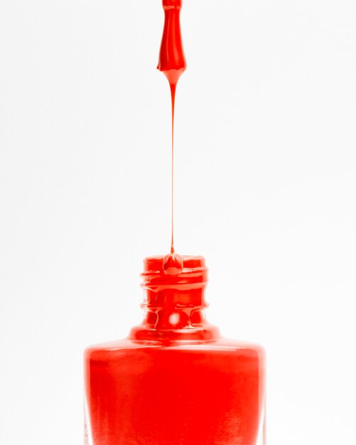 Belo vermelho colorido esmalte pingando do pincel em garrafa em pano de fundo branco