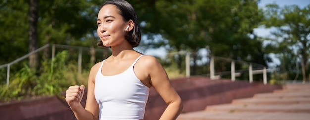 Foto grátis bem-estar e esporte corredor de fitness asiático correndo no parque correndo na rua em leggings sorrindo