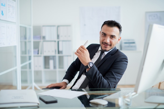 Bem sucedido empresário caucasiano sentado na mesa no escritório e sorrindo