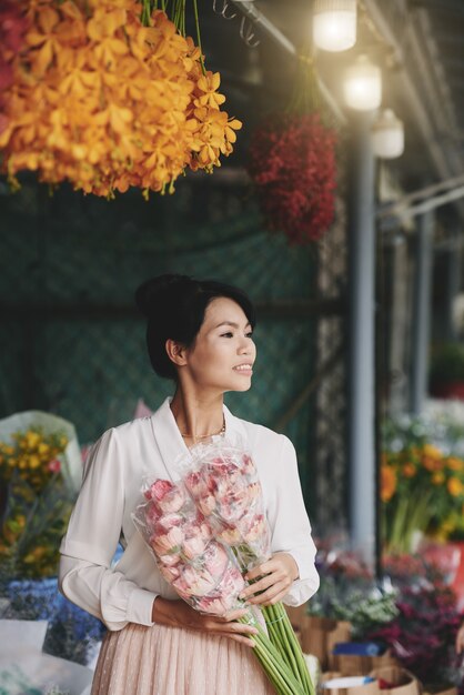 Bem vestida linda mulher asiática posando com flores frescas no mercado