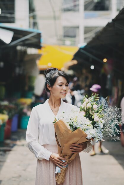 Bem vestida mulher asiática andando pelo mercado e carregando buquê de flores grande