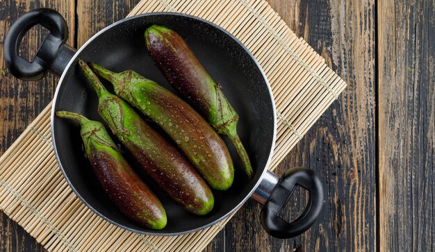 Berinjelas verdes em uma panela em madeira e placemat,