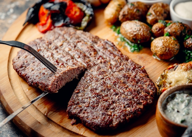 bife com batatas fritas e legumes na placa de madeira