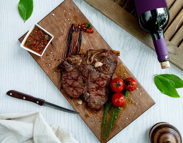 Bife de borrego servido com molho, tomate grelhado