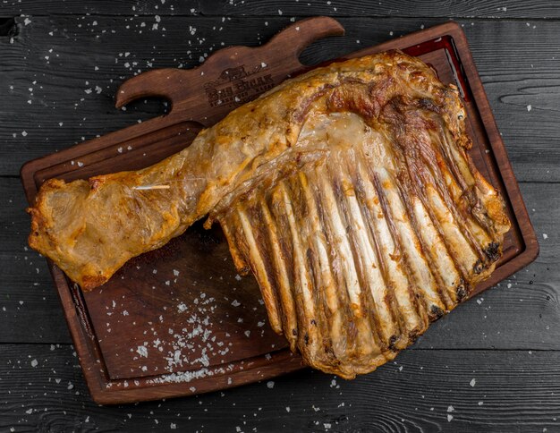 Bife de carne inteira com ossos em uma placa de madeira.