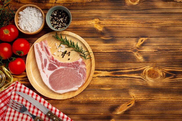 Bife de costeleta de porco crua na superfície de madeira escura.