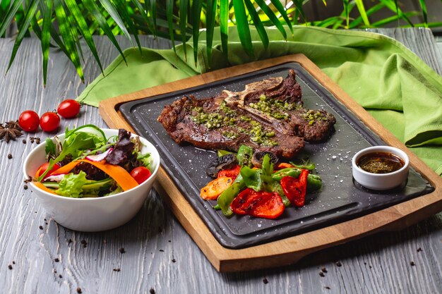 Bife de osso de vista lateral com legumes grelhados e molho no quadro com salada de legumes