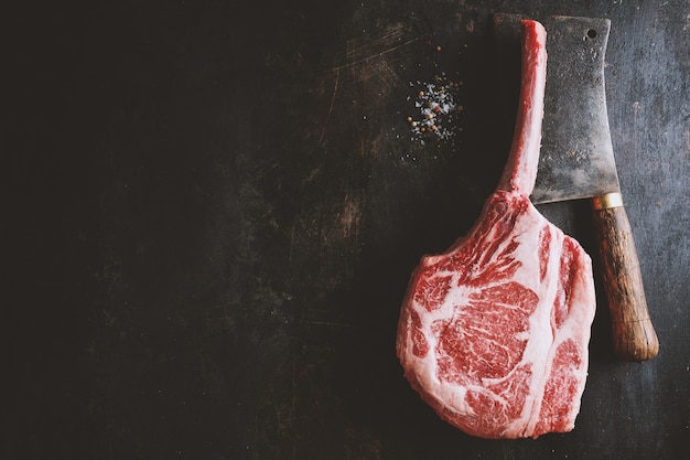 Bife de tomahawk de carne fresca na prancha de madeira velha. Fundo escuro. Fechar-se